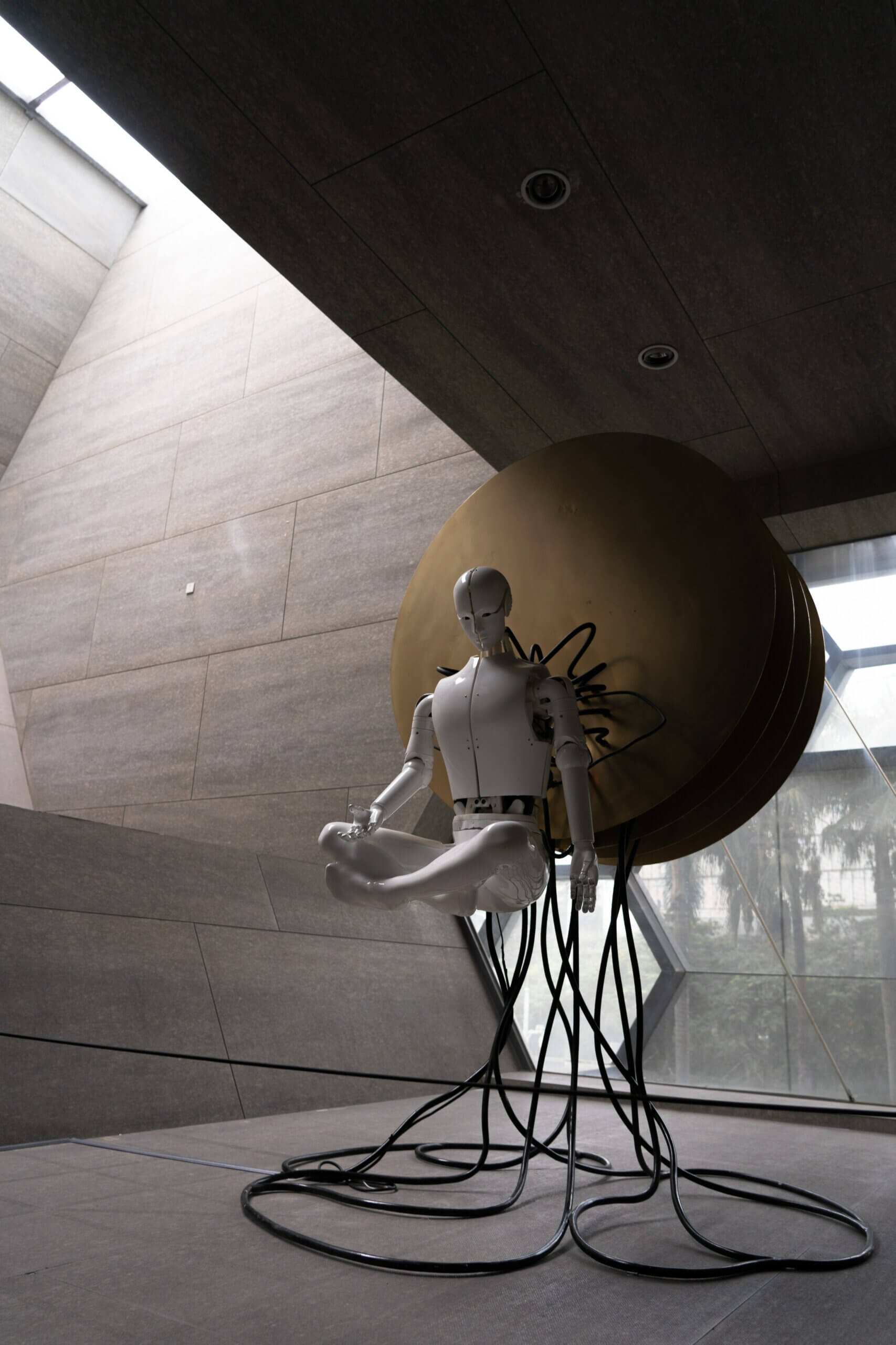 Ein schwebender Roboter mit Kabeln verbunden in einem futuristischen Raum vor einer bronzenen schwebenden Scheibe.