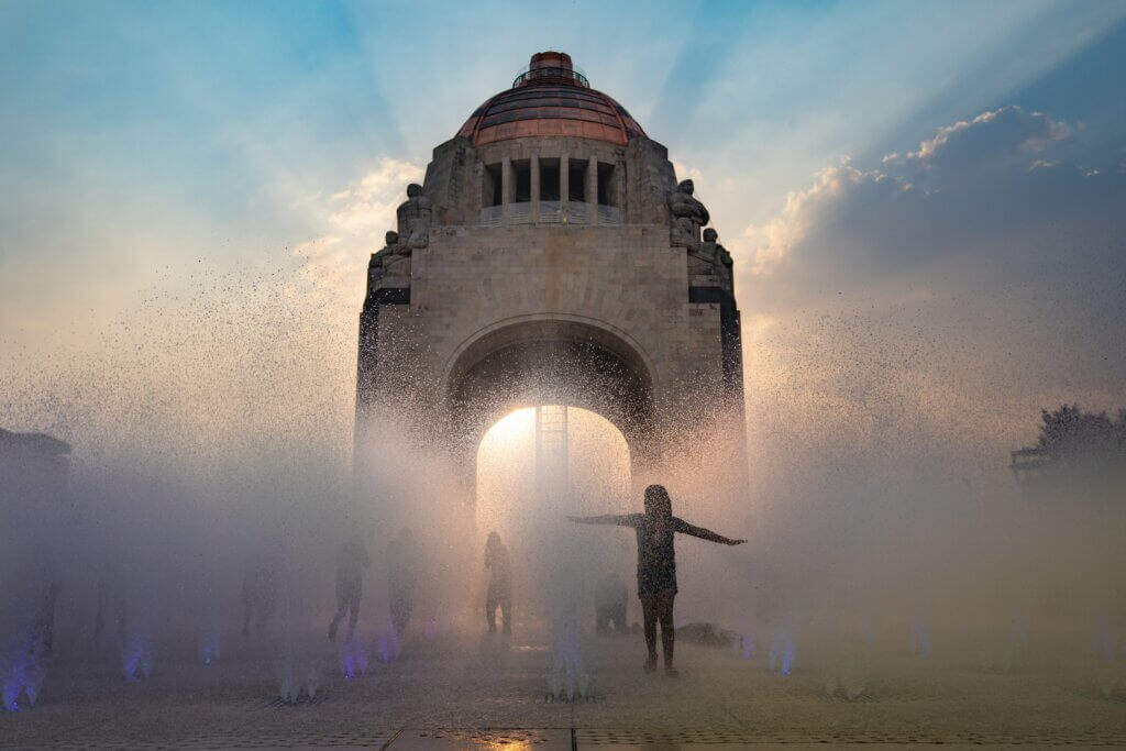 Wasserfontänen in Gegenlicht auf einem öffentlichen Platz aufgenommen. Menschen als Schatten zu erkennen, genießen das Wasser.