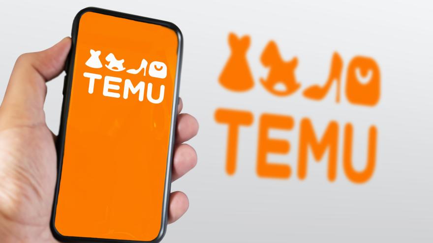 Ein Handy mit dem Logo von TEMU ist zu sehen, dahinter das Logo in Groß auf einer Wand